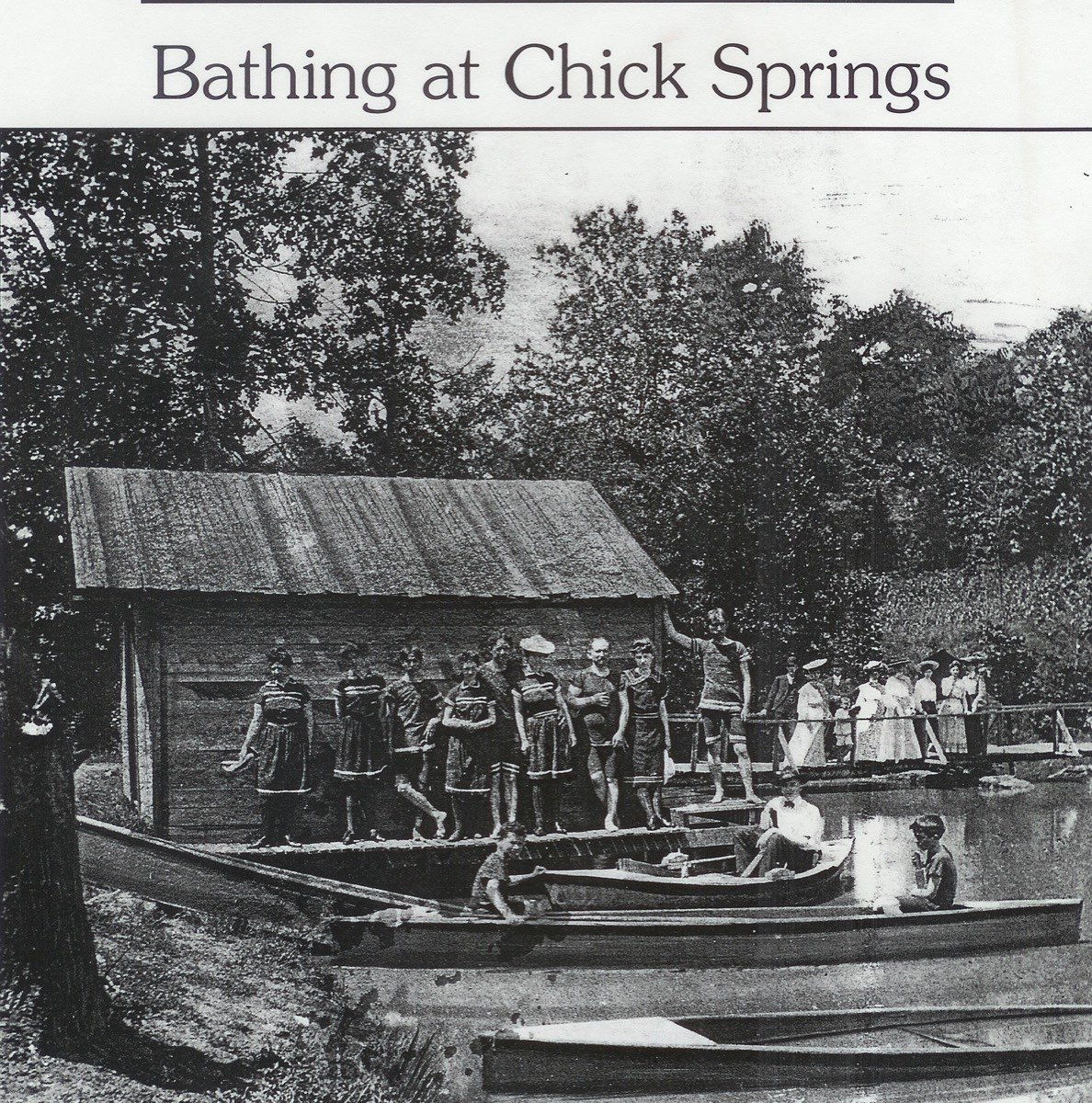 A group of men, women, and children gathered around a rustic wooden building at the springs