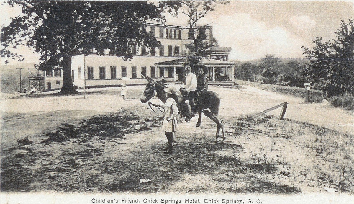 Adults and a child with a donkey in front of the three-story Chick Springs Hotel, c. 1903–1907